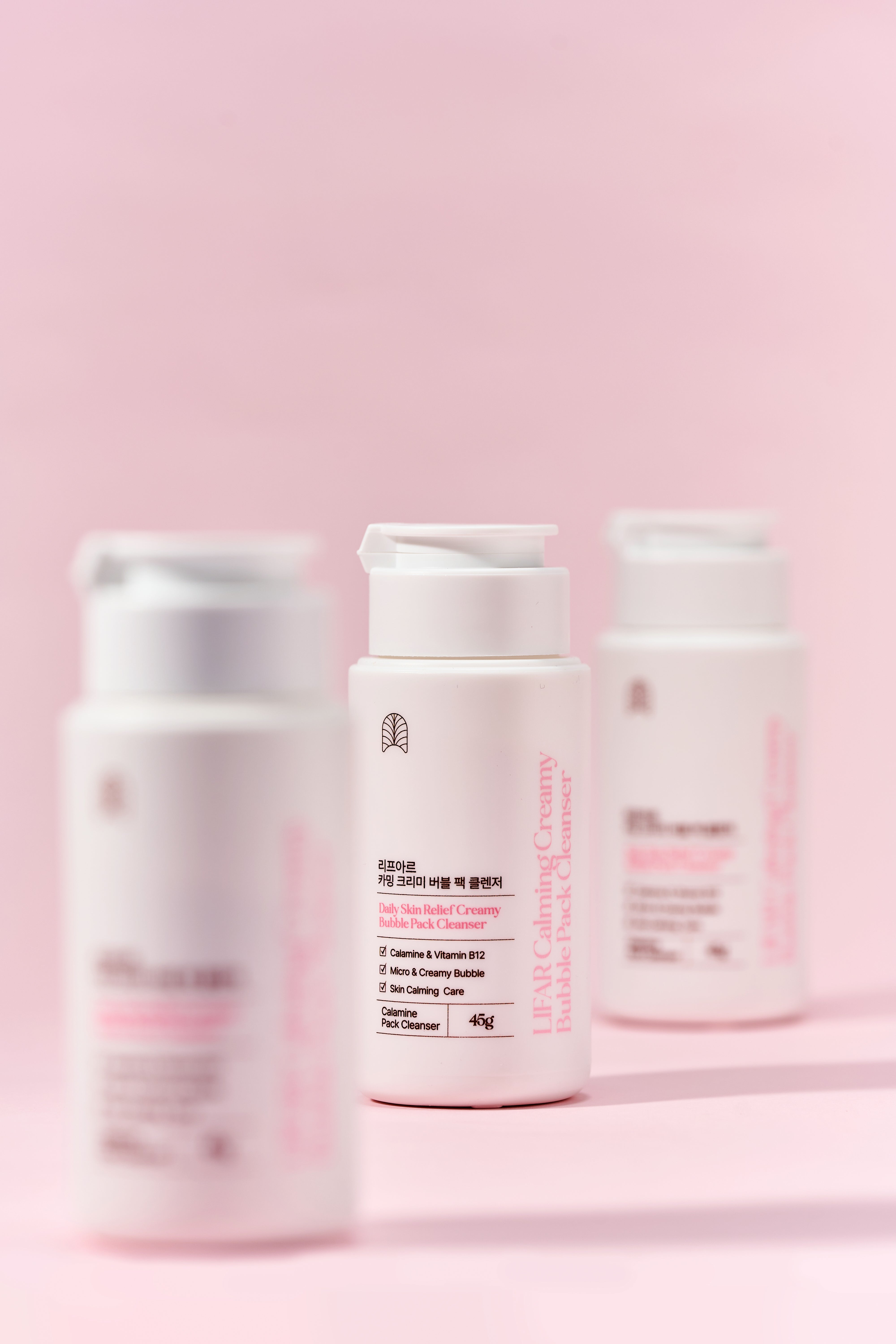 Three skincare bottles on a pink background