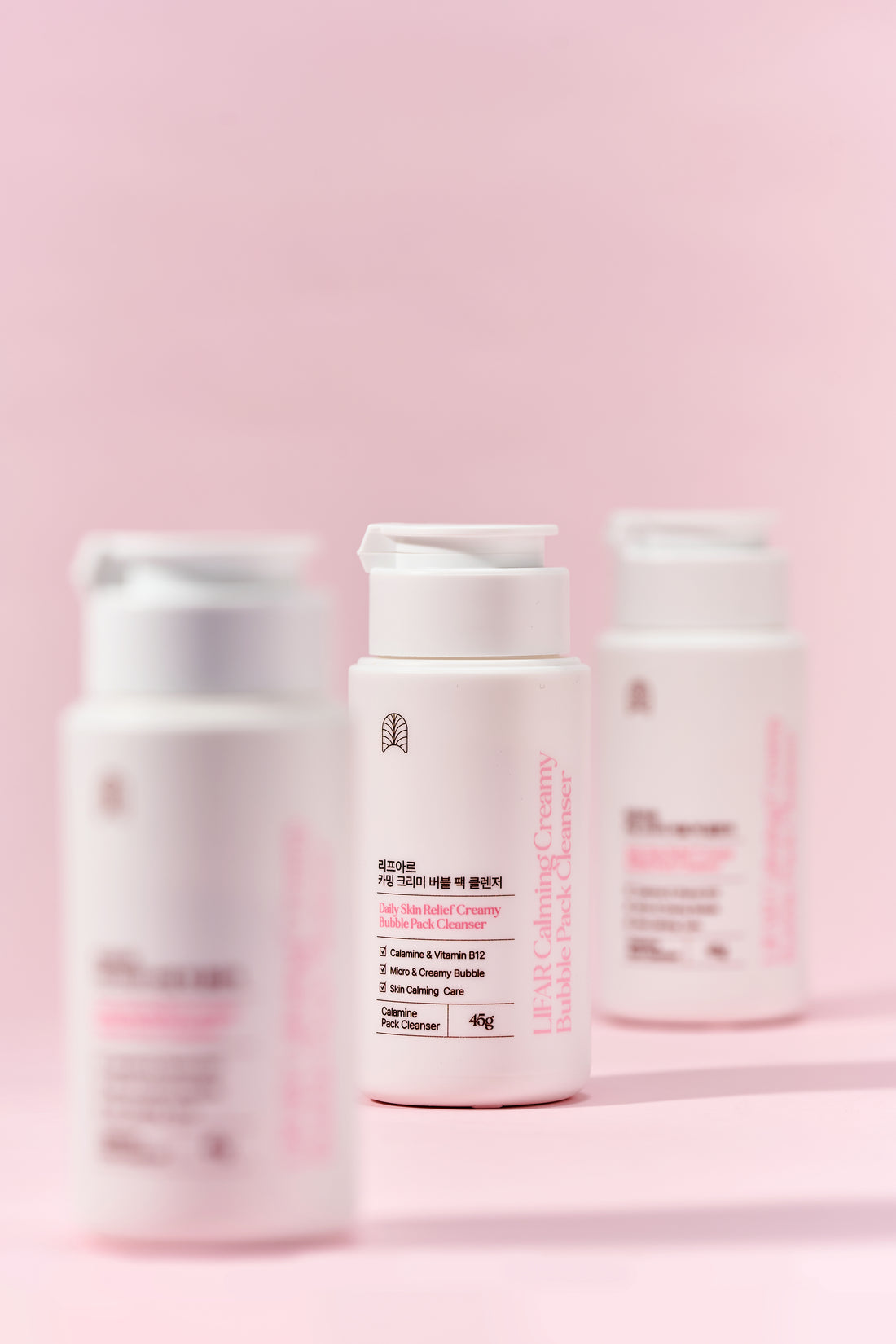 Three skincare bottles on a pink background