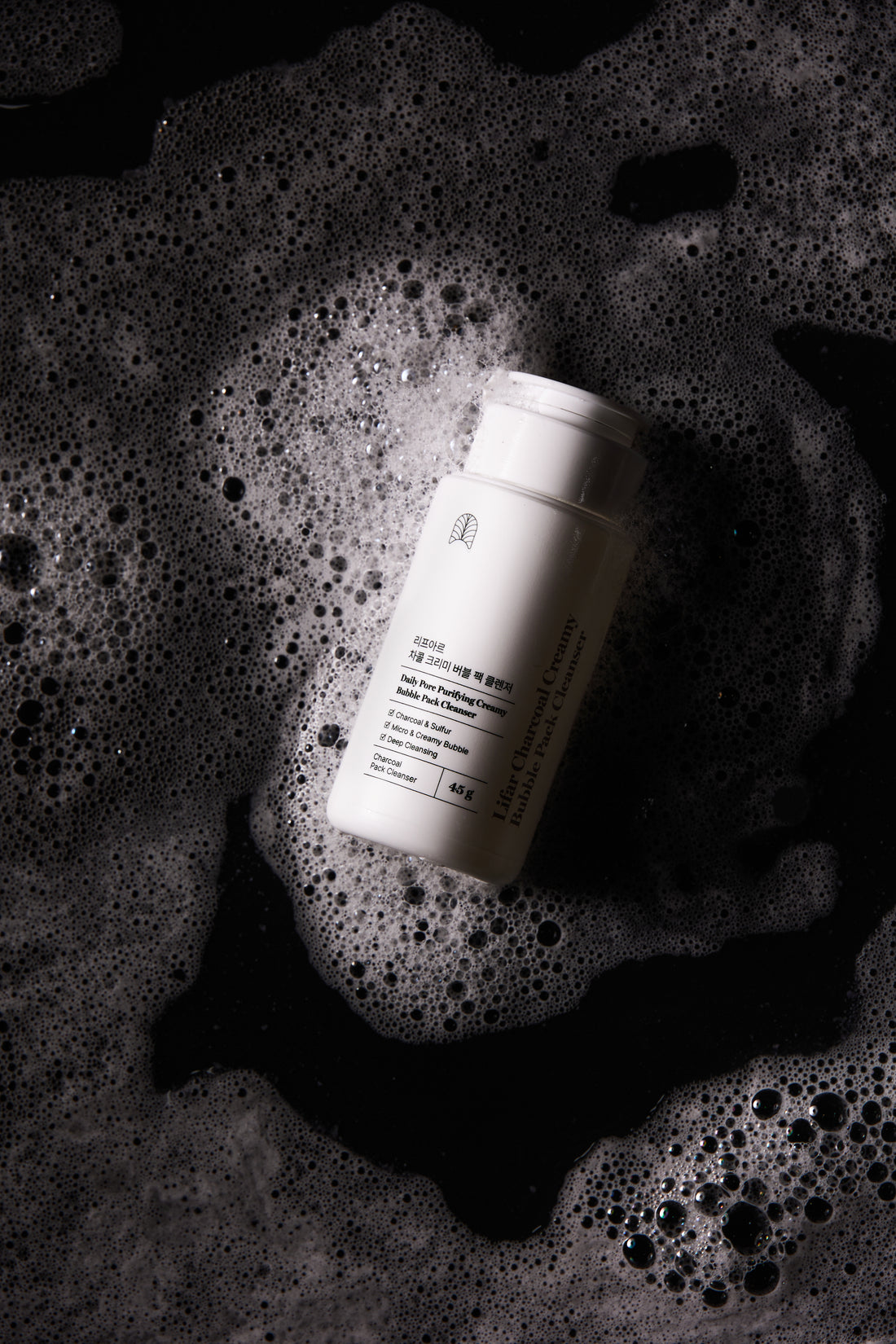 White bottle with label on a textured black surface with bubbles